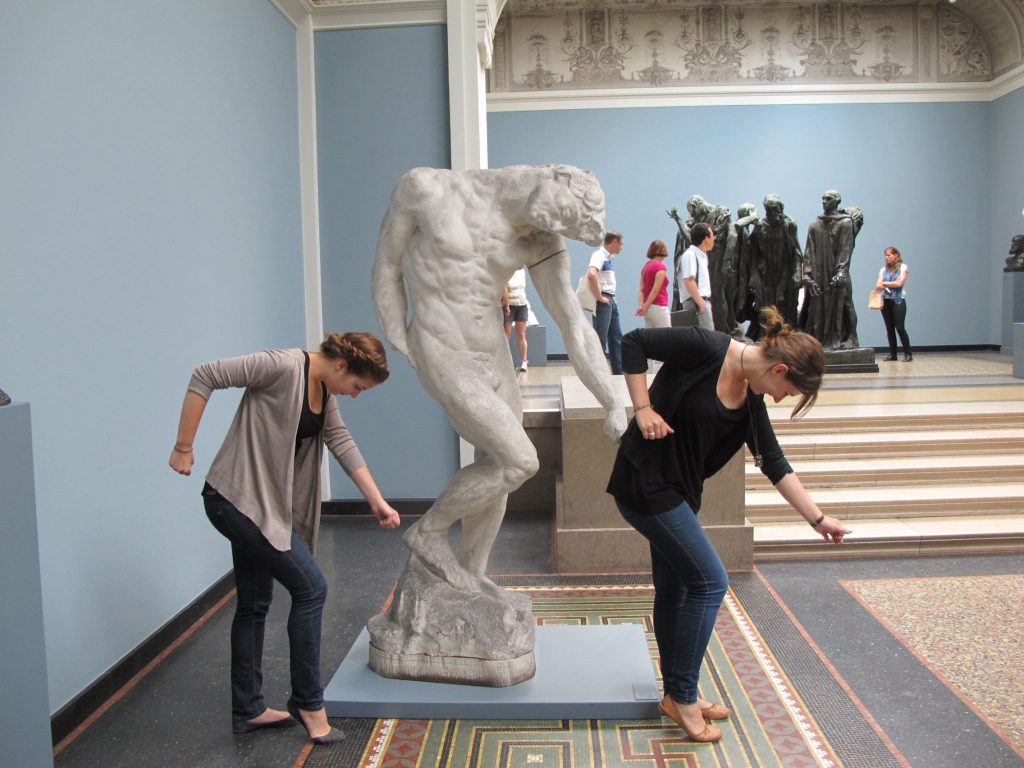 Two ladies do the Beyonce single ladies dance next to a statue doing the same pose.